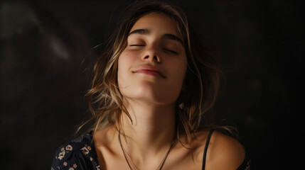 Portrait of a content young woman with closed eyes, enjoying a peaceful moment on a dark background.