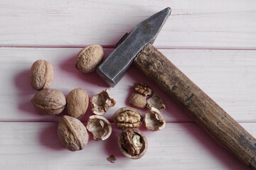 Walnuts, whole and peeled, on a pink wooden background next to a hummer.