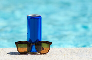 Sunglasses and a can of cold, refreshing drink on a hot day. Resort pool and cold drink. Free space.