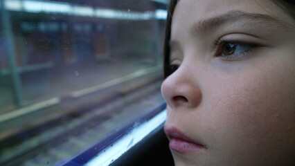 Thoughtful child close-up face leaning on train window staring at platform station arrival. Macro...