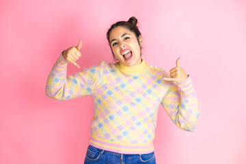 Young beautiful woman wearing casual sweater over isolated pink background shouting with crazy expression doing rock symbol with hands up