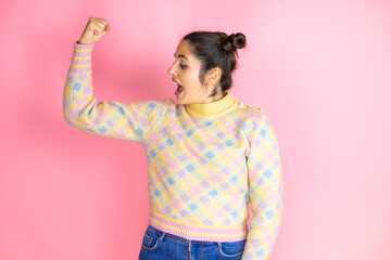 Young beautiful woman wearing casual sweater over isolated pink background showing arms muscles...