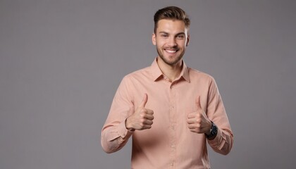 A man with stubble giving two thumbs up and a confident smile, wearing a pink shirt against a grey background.