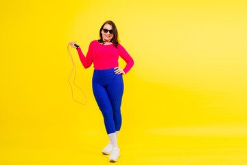 Pretty smiling plump female in sporty top and leggings holding jumping rope in hands