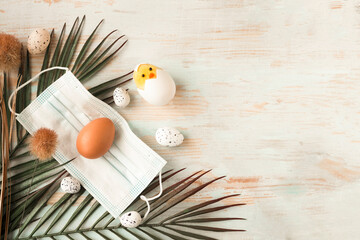 Chicken egg in face medical mask, palm branch and toy chicken. Easter holiday during the...
