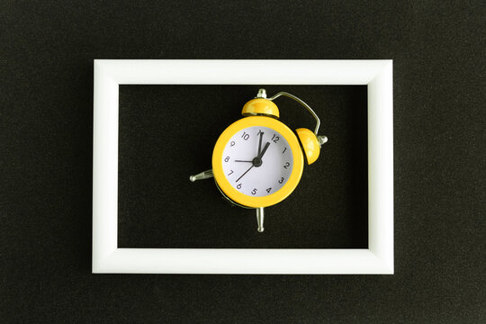 Alarm clock and white photo frame on black background. Minimal concept