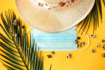 Straw hat and face medical mask on yellow background. Top view. Travel during the coronavirus...