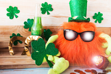 Toy leprechaun with ginger beard in green hat and sunglasses holds a shamrock in his hands. Saint...