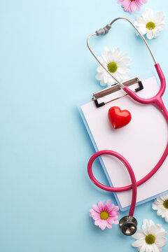 Nurturing wellness: a heartfelt approach to health. Top view vertical shot of clipboard, red heart, pink stethoscope, mix of white and pink flowers on light blue background with space for warm wishes.