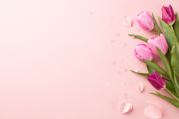 Joyful blossoms: crafting memorable greetings for spring festivities. Top view shot of pink tulips and heart-shaped paper decorations on pastel pink background with space for advertising