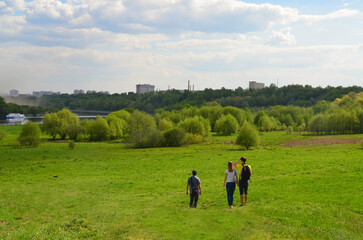 Group of young people is relaxing in a summer park. Beautiful spring landscape, bright sunny day. Kolomenskoye, Moscow.