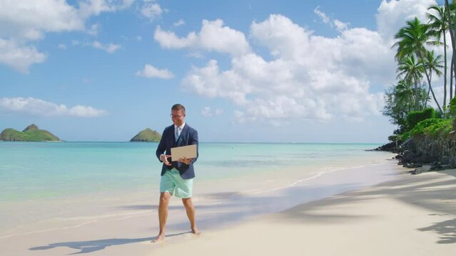 Extremely happy workaholic celebrating success, clenching fist with victory, standing barefoot on white sand washed by crystal clear waters of the ocean. High quality 4k footage