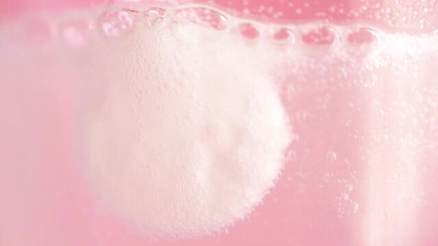 View of a blurred effervescent tablet dissolving in water with a pink background. Blurred pill dissolves in water. Medicine. Macro.