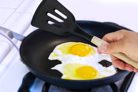 hand holding a Slotted Turner with eggs in a frying pan