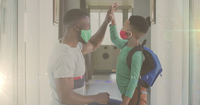 Image Of Lights Over Happy African American Father And Son In Face Masks And Clapping Hands