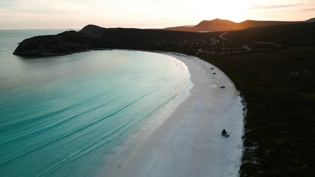 drone shot over Lucky Bay in Cape Legrand National Park at sunset wth 4WD on the beach and the sun in the background, Western Australia
