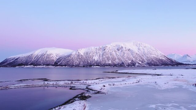Majestic snowy mountain in front of icy fjord in Norway. The sky sinks into pink and blue. Arial Drone Shot