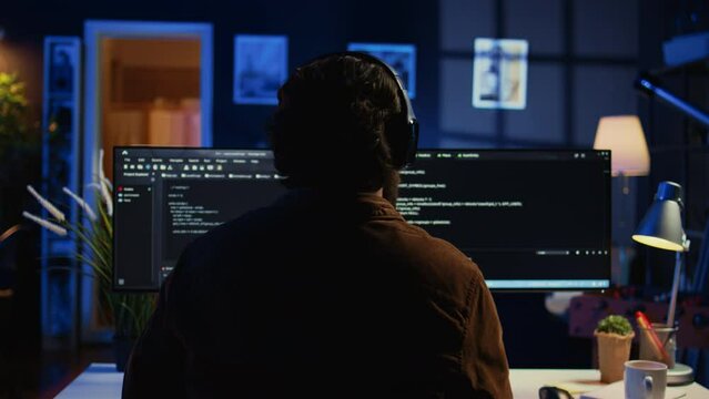 Technician putting headphones on while using coding to fortify firewalls, teleworking for IT company. Computer scientist listening music and upgrading binary code scripts in home office, camera B