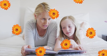 Image of flowers over caucasian mother and daughter reading book in bed