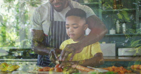 Image of leaves over happy african american father and son cooking together