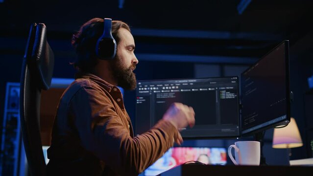 Cheerful programmer listening music while doing web development during remote job shift in neon lit home office, finishing coding project. IT expert enjoying audio podcast, working on PC, camera B