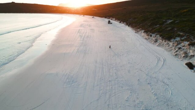 reveal shot of a motorcycle driving on Lucky Bay in Cape Legrand national park at sunset, western australia