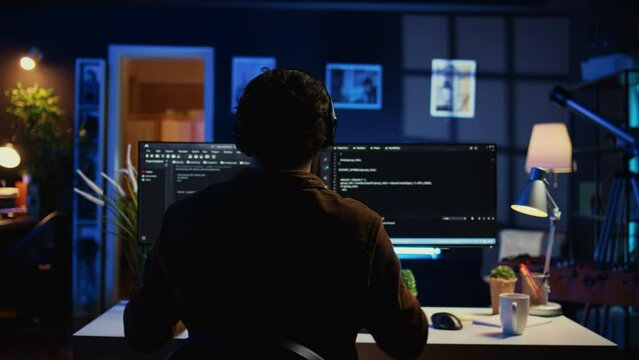 Engineer wearing headphones while using coding to fortify security, remotely working for IT company. Software expert listening music and upgrading binary code scripts on computer, camera B