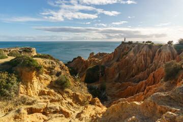 Tourist standing on golden rock cliffs at the coastline of the Atlantic Ocean with near the Cave of...