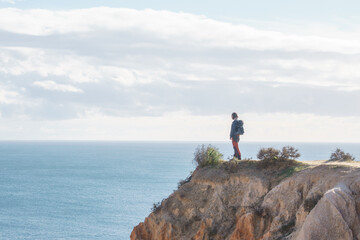 Fototapeta premium Tourist standing on golden rock cliffs at the coastline of the Atlantic Ocean with near the Cave of Benagil, Algarve, Portugal