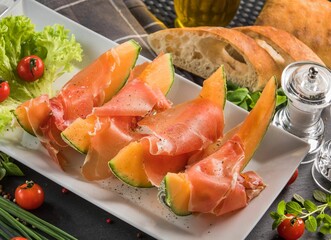 White plate featuring prosciutto ham with melon cantaloupe slices.