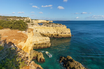 Boat on the sea in front of the golden cliffs at the atlantic coast line near Benagil cave, Algarve, Portugal.