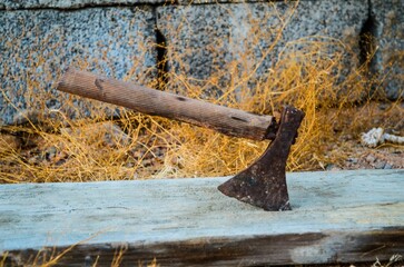 a dirty axe stuck in a wood beam next to some dry grass