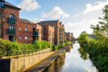 Brick apartment buildings and converted warehouses in a redevelopment along a canal at sunset. Afootpath lines the canal. - obrazy, fototapety, plakaty