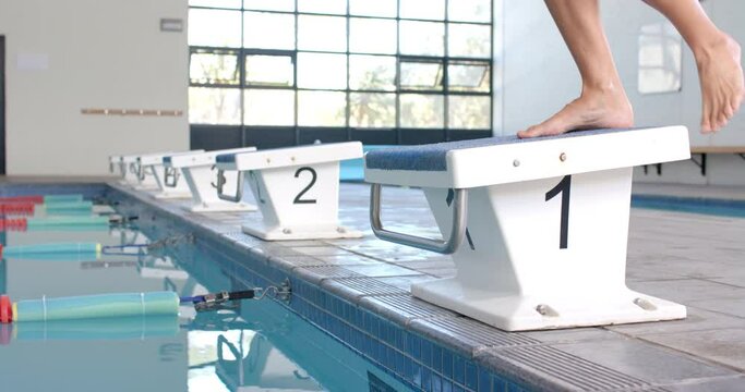 Person stands on a starting block at a swimming pool, with copy space