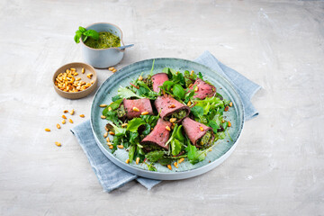 Traditional mixed salad with spinach filled roast beef rolls and pine nuts served as a close-up on a design plate with text space