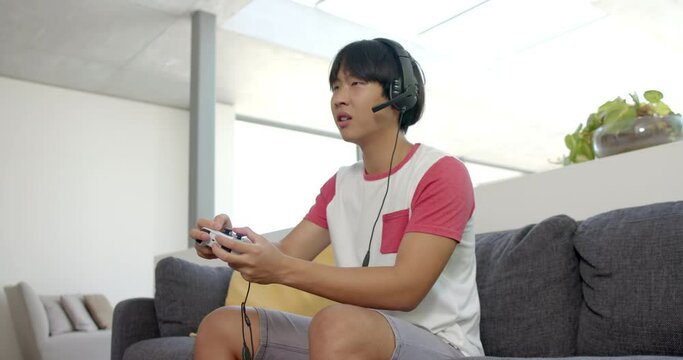 Teenage Asian boy plays video games in a home setting with copy space