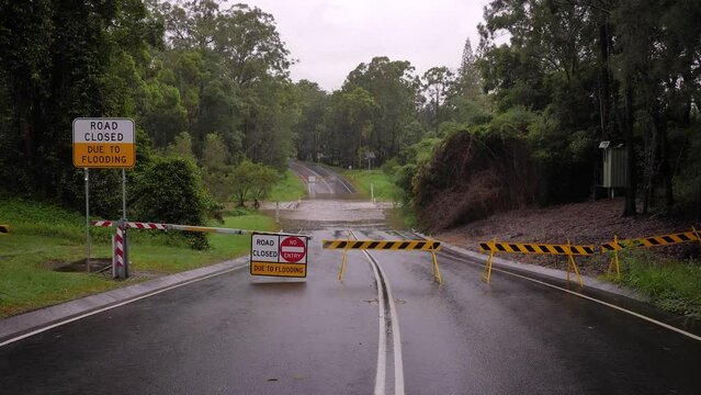Gold Coast, Queensland, 16 February 2024 - Wide shot of road closure signage with flooding across Hardy's Road in Mudgeeraba after heavy rains continue to lash South East Queensland, Australia.