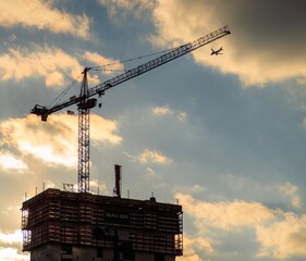 Plane passing construction crane at sunset