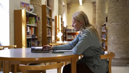 Middle aged Teacher getting ready for a school lesson. Create Curriculum for students in library. Woman Tutor make plans and notes, Education development subject using laptop and internet