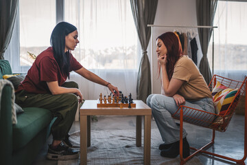 two women young females sisters friends play chess board game at home