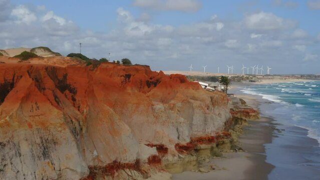 Aerial view of the sea, waves, cliffs, a small village and a wind energy at background, Morro Branco, Ceara, Brazil