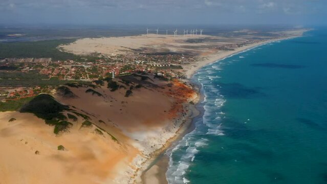 Aerial view of the sea, waves, cliffs, a small village and a wind energy at background, Morro Branco, Ceara, Brazil