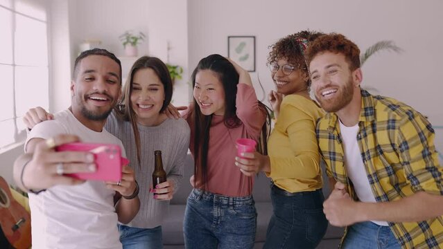 Young group of millennial students enjoying home party. Diverse friends dancing and drinking beer while listening music at shared flat. 