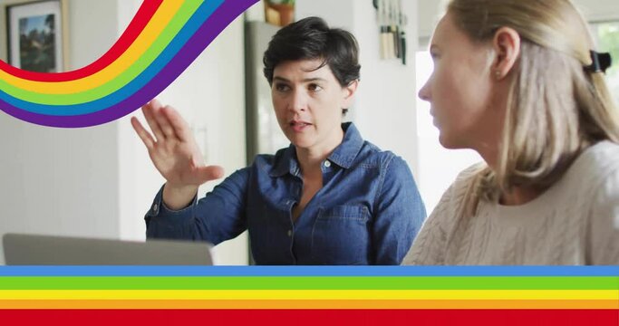 Animation of pride rainbow stripes over happy caucasian lesbian couple using laptop and talking