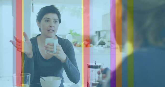 Animation of pride rainbow stripes over caucasian lesbian couple talking at breakfast