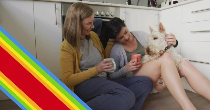Animation of pride rainbow stripes and hand over caucasian lesbian couple in kitchen with pet dog