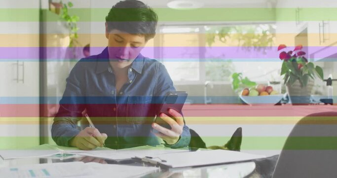 Animation of pride rainbow stripes over caucasian using smartphone working in kitchen with pet dog