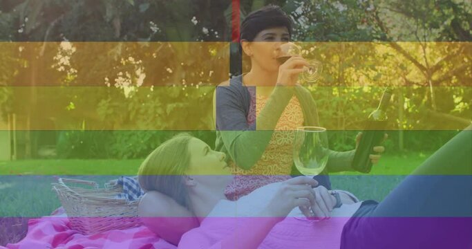 Animation of pride rainbow stripes over happy caucasian lesbian couple drinking wine in sunny garden