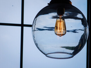 a clear light bulb hanging from a ceiling lamp near a window