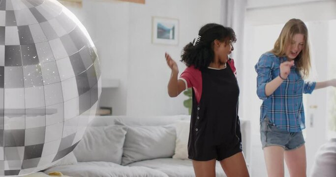 Animation of mirror ball over two diverse teenage girls having fun dancing at home